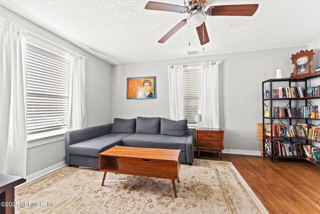 living room featuring hardwood / wood-style flooring, ceiling fan, and a textured ceiling