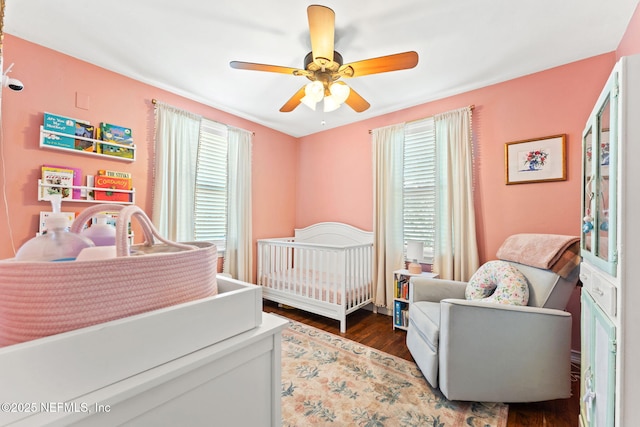 bedroom with ceiling fan, dark hardwood / wood-style flooring, and a crib