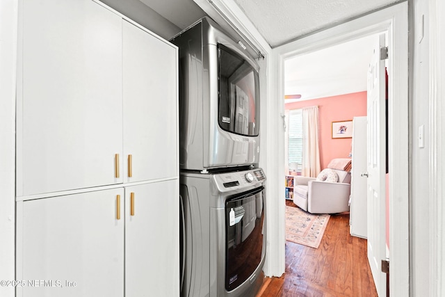 washroom featuring cabinets, hardwood / wood-style floors, a textured ceiling, and stacked washer and clothes dryer