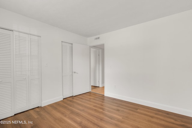 unfurnished bedroom with wood-type flooring and two closets