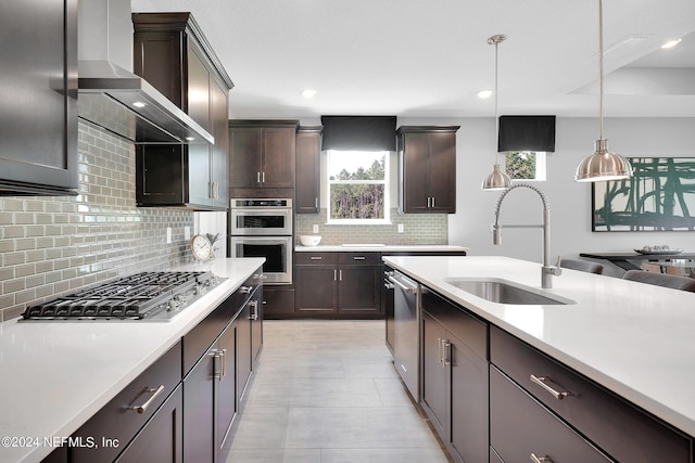 kitchen featuring pendant lighting, sink, wall chimney exhaust hood, appliances with stainless steel finishes, and dark brown cabinets