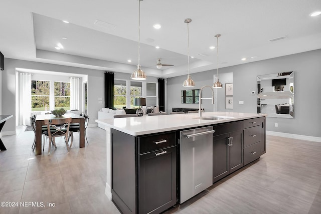 kitchen with a raised ceiling, a kitchen island with sink, sink, and hanging light fixtures