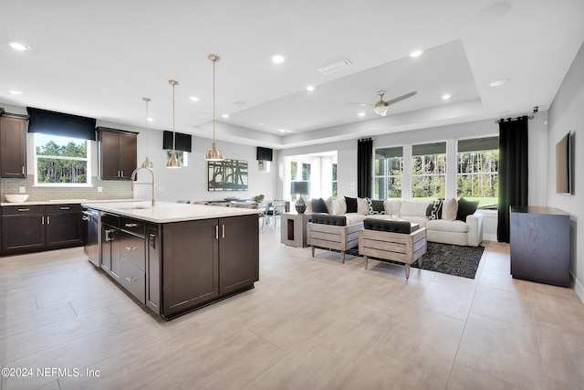 kitchen with a raised ceiling, sink, ceiling fan, an island with sink, and decorative light fixtures