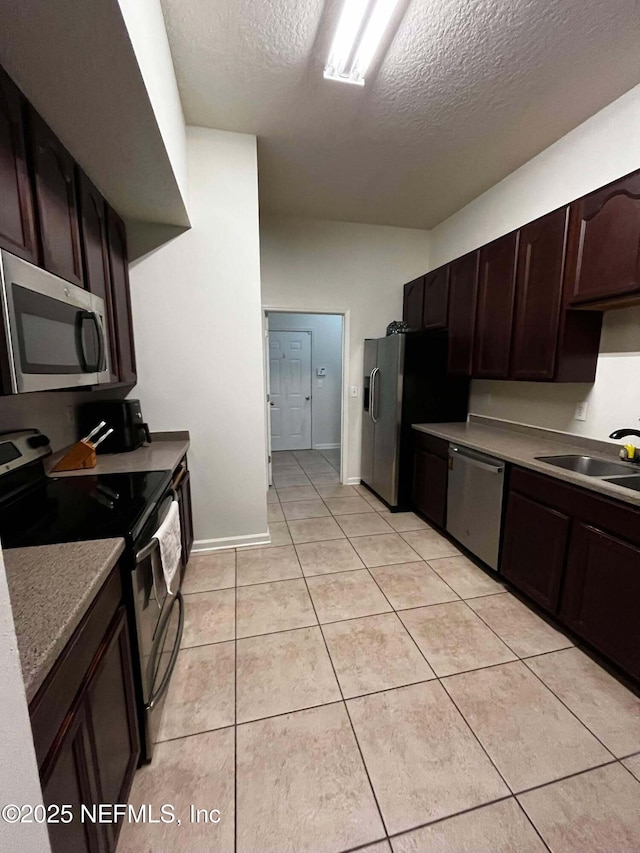 kitchen featuring sink, light tile patterned floors, appliances with stainless steel finishes, dark brown cabinets, and a textured ceiling