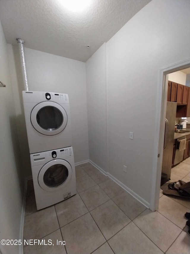 laundry room featuring stacked washing maching and dryer, light tile patterned flooring, and a textured ceiling