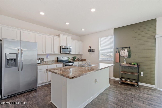 kitchen featuring light stone countertops, stainless steel appliances, a kitchen island with sink, sink, and white cabinetry