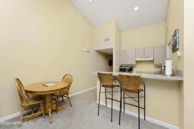 kitchen with gray cabinetry, a kitchen breakfast bar, vaulted ceiling, light colored carpet, and kitchen peninsula