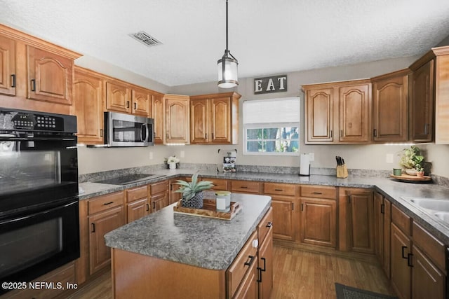 kitchen with a textured ceiling, black appliances, a center island, light hardwood / wood-style floors, and hanging light fixtures