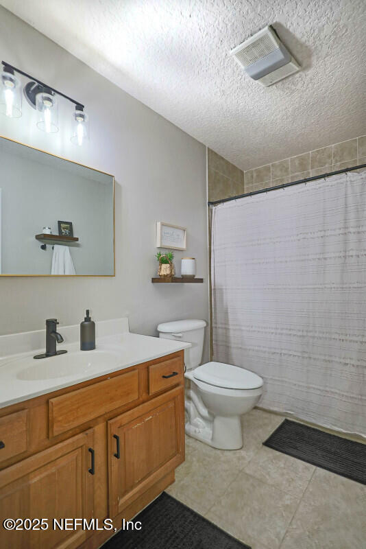 bathroom with vanity, toilet, a textured ceiling, and walk in shower