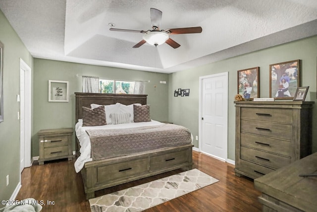 bedroom featuring ceiling fan, dark hardwood / wood-style flooring, a raised ceiling, and a textured ceiling