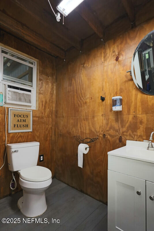 bathroom featuring vanity, wood walls, toilet, beamed ceiling, and wood-type flooring