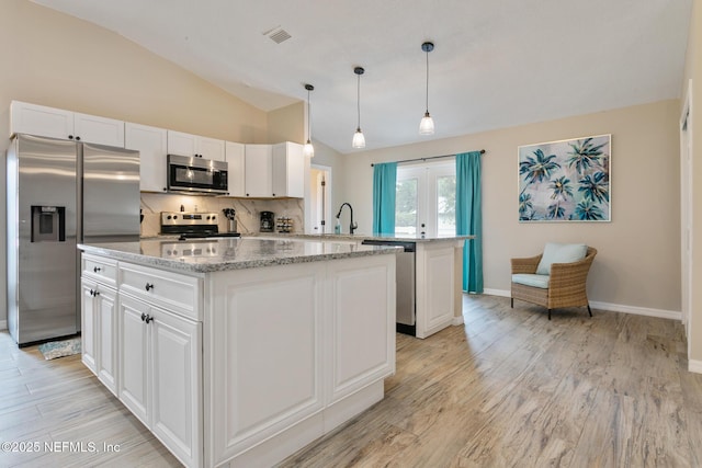 kitchen with appliances with stainless steel finishes, a kitchen island, white cabinetry, and lofted ceiling