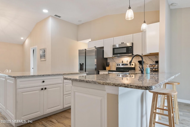 kitchen with pendant lighting, a center island, white cabinets, light wood-type flooring, and stainless steel appliances