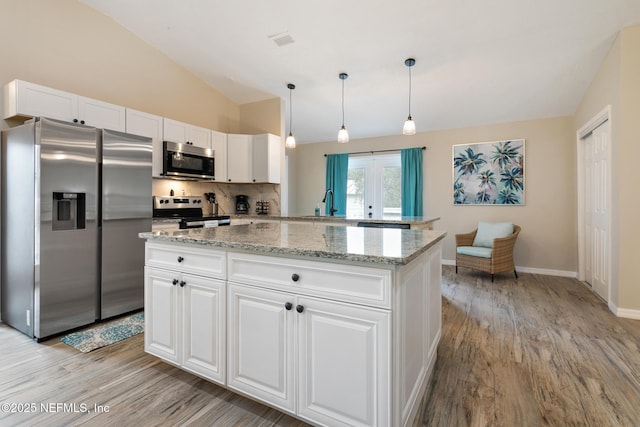 kitchen featuring stainless steel appliances, vaulted ceiling, pendant lighting, light hardwood / wood-style flooring, and white cabinetry