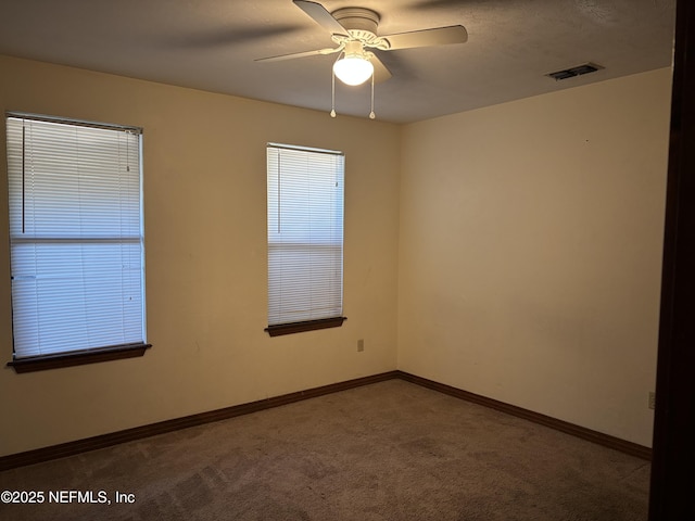 carpeted spare room with baseboards, visible vents, and ceiling fan