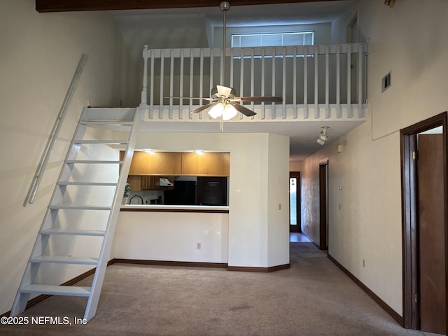 unfurnished living room featuring a ceiling fan, visible vents, baseboards, a towering ceiling, and carpet flooring