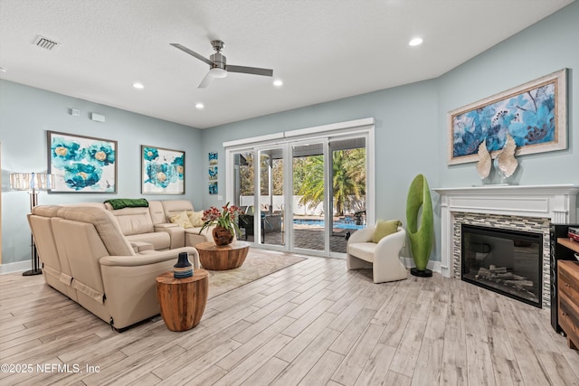 living room featuring ceiling fan, a fireplace, a textured ceiling, and light hardwood / wood-style flooring