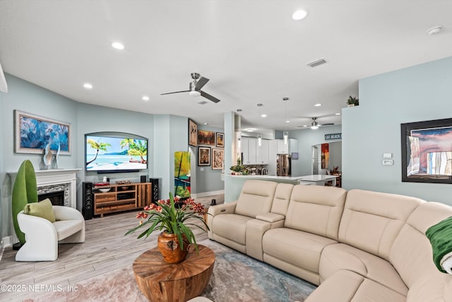 living room featuring a fireplace, ceiling fan, and light hardwood / wood-style flooring