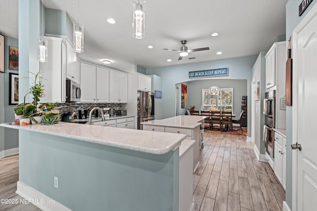 kitchen with hanging light fixtures, ceiling fan, appliances with stainless steel finishes, a kitchen island, and kitchen peninsula