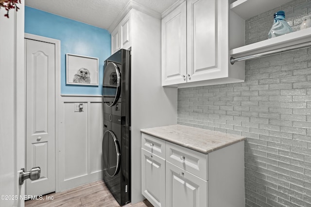 laundry area with a textured ceiling, cabinets, and stacked washer / dryer