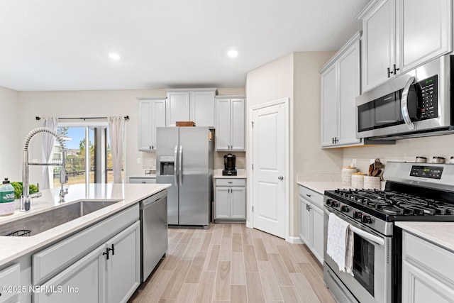 kitchen with appliances with stainless steel finishes, white cabinetry, light hardwood / wood-style floors, and sink