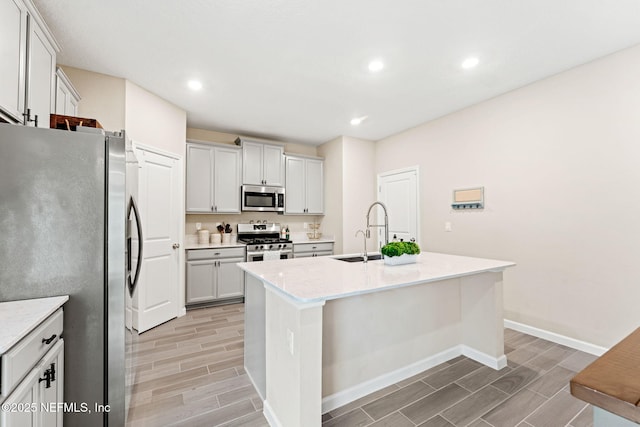 kitchen featuring white cabinets, stainless steel appliances, an island with sink, light stone countertops, and sink