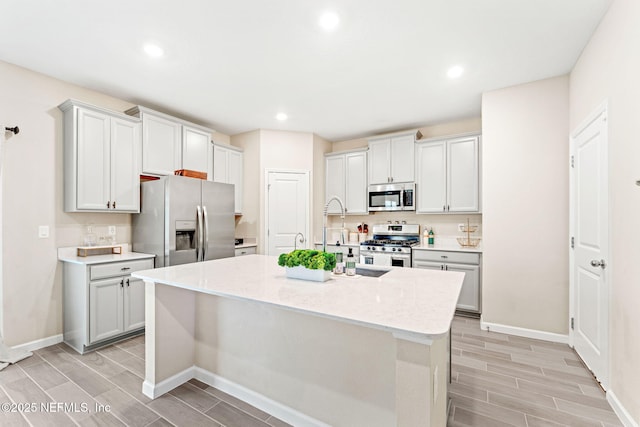 kitchen featuring stainless steel appliances, a kitchen island with sink, and light stone countertops