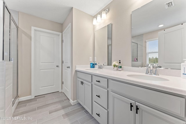 bathroom with a textured ceiling, vanity, and a shower with shower door