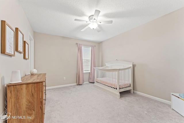 unfurnished bedroom with ceiling fan, light colored carpet, a textured ceiling, and a nursery area