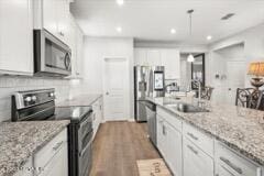 kitchen with sink, stainless steel appliances, light stone counters, dark hardwood / wood-style flooring, and white cabinets