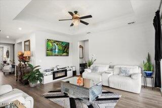 living room featuring hardwood / wood-style floors, ceiling fan, and a raised ceiling