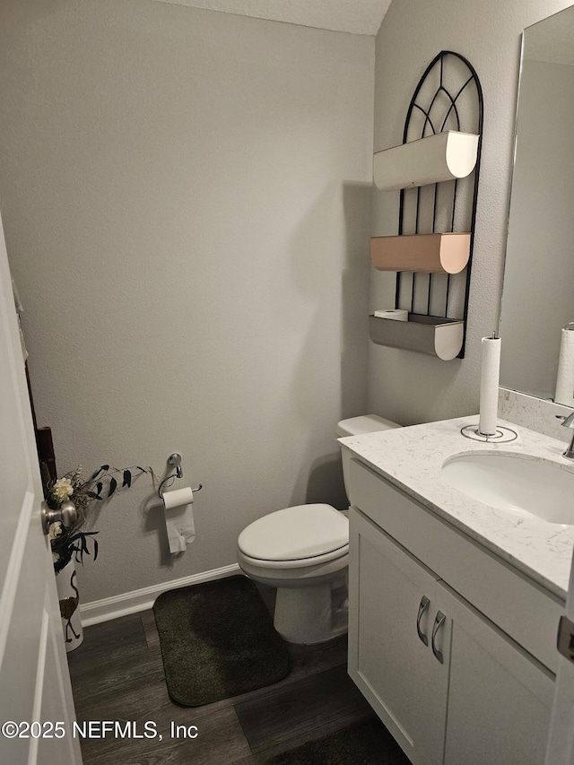 half bath featuring baseboards, vanity, toilet, and wood finished floors