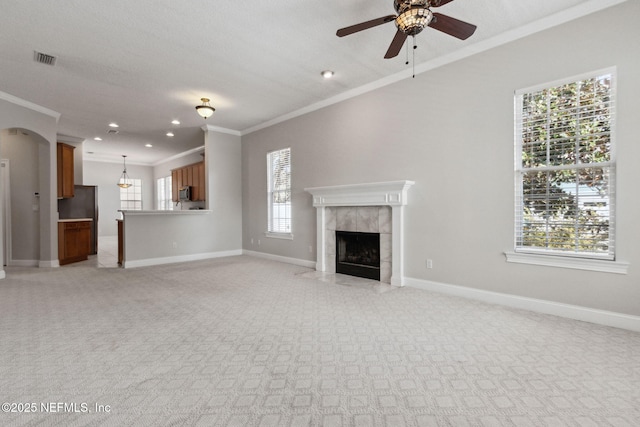 unfurnished living room featuring a healthy amount of sunlight, ceiling fan, ornamental molding, and a tiled fireplace