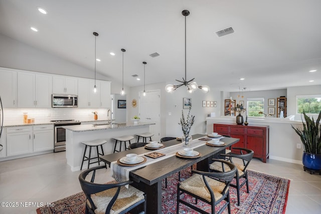 dining room with sink, light tile patterned floors, vaulted ceiling, and a notable chandelier