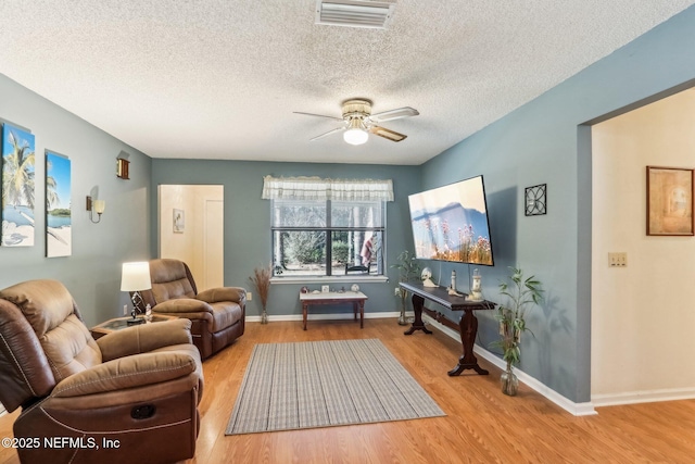 living area with a textured ceiling, ceiling fan, and light hardwood / wood-style flooring