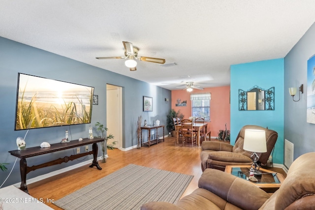 living room with ceiling fan, a textured ceiling, and light wood-type flooring