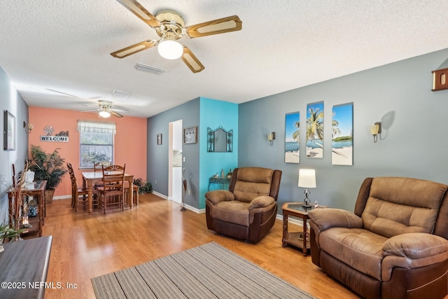 living room featuring ceiling fan, light hardwood / wood-style floors, and a textured ceiling