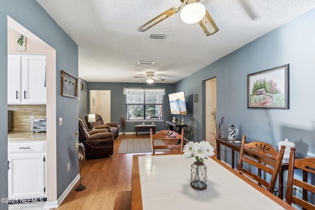 dining room with ceiling fan, light wood-type flooring, and a textured ceiling