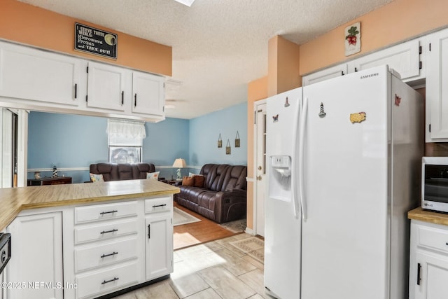 kitchen featuring white cabinetry, light tile patterned floors, a textured ceiling, and white fridge with ice dispenser