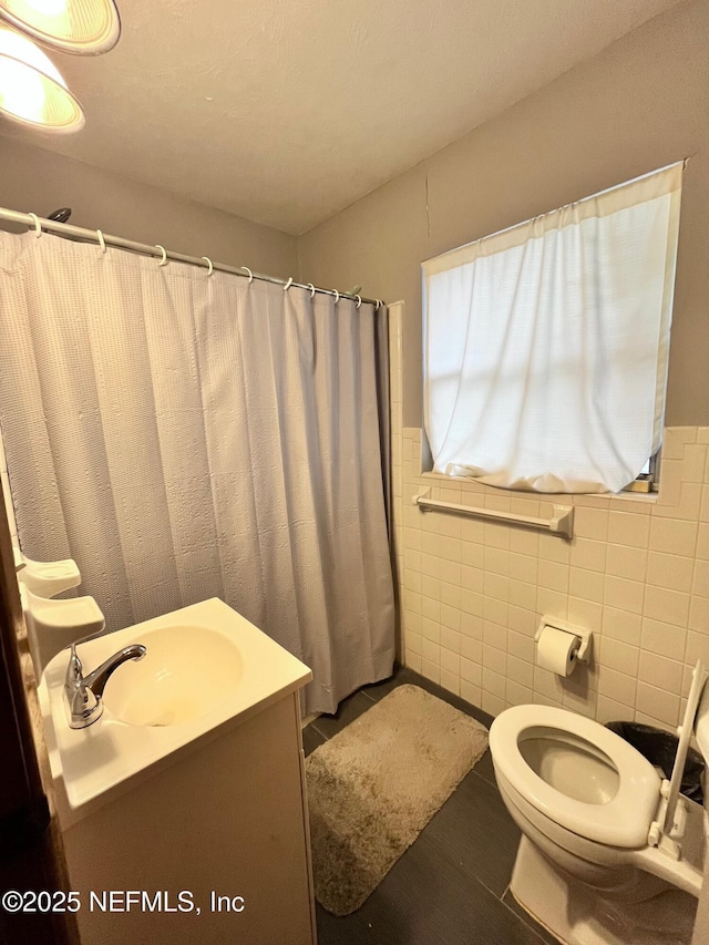 bathroom with tile walls, toilet, vanity, and a shower with shower curtain