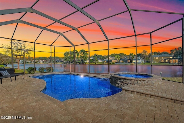 pool at dusk featuring a patio, an in ground hot tub, glass enclosure, and a water view