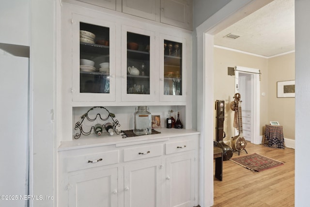 bar with light hardwood / wood-style flooring, white cabinets, ornamental molding, and white refrigerator