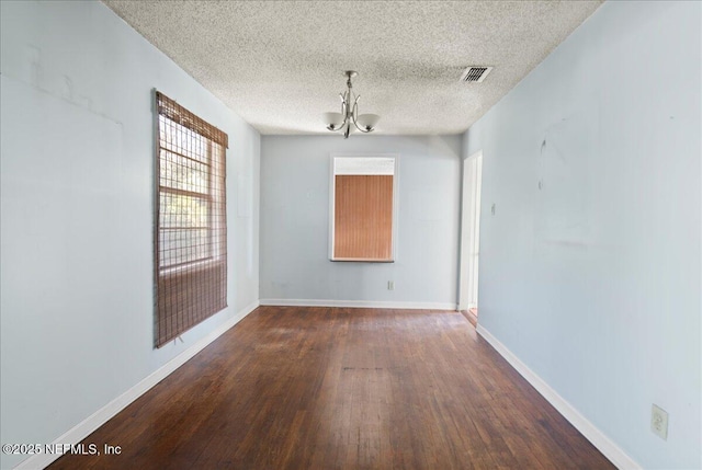 empty room with dark wood-type flooring, a textured ceiling, and a chandelier