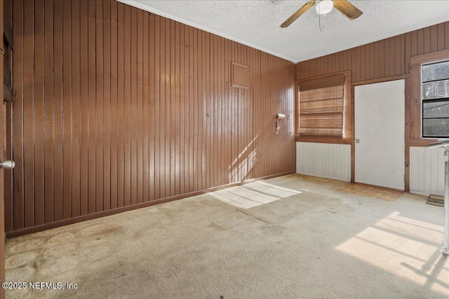 carpeted spare room featuring a textured ceiling, ceiling fan, and wooden walls