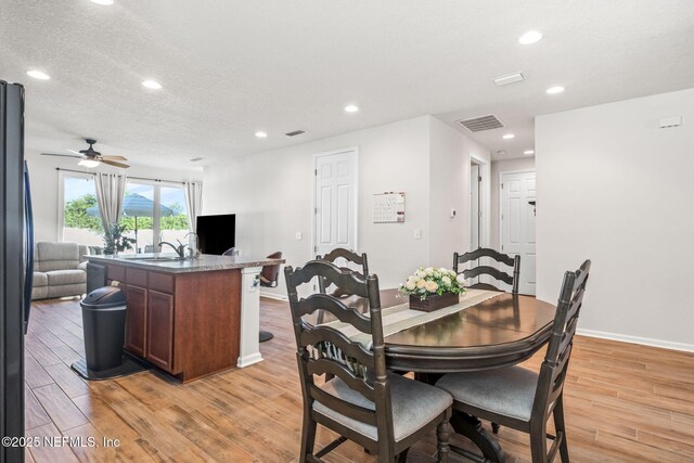 dining space featuring a textured ceiling, light hardwood / wood-style flooring, ceiling fan, and sink