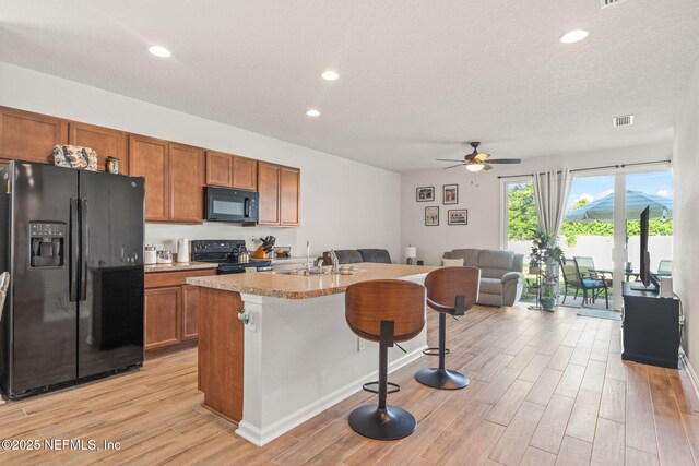 kitchen with a breakfast bar, black appliances, a center island with sink, sink, and light wood-type flooring