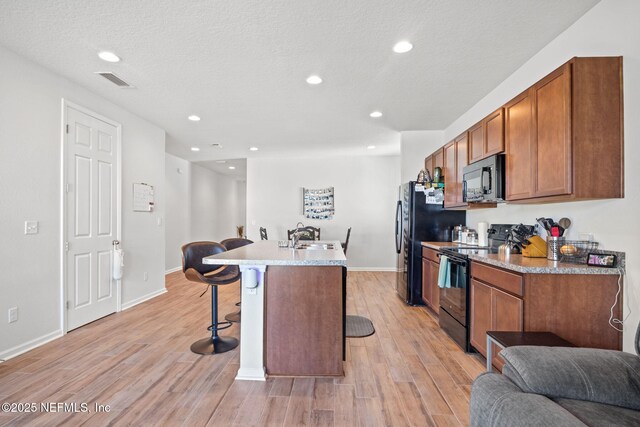 kitchen with a breakfast bar, a kitchen island with sink, sink, black appliances, and light hardwood / wood-style floors