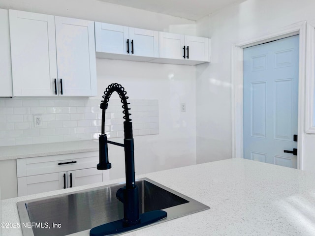 kitchen featuring white cabinets, decorative backsplash, light stone counters, and sink