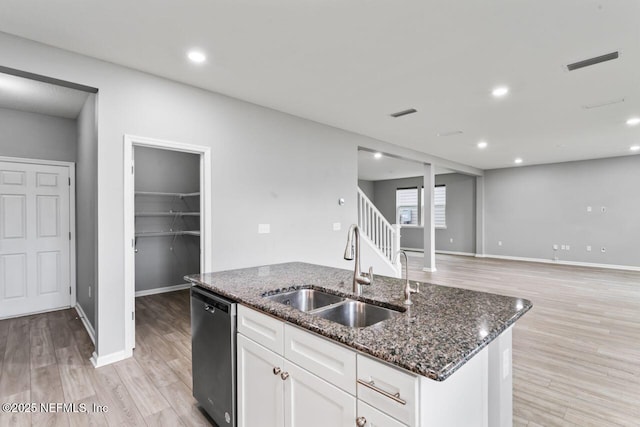 kitchen featuring dishwasher, dark stone counters, white cabinets, sink, and an island with sink