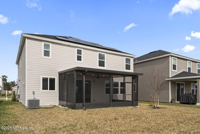 rear view of property with central AC unit, solar panels, a sunroom, and a lawn